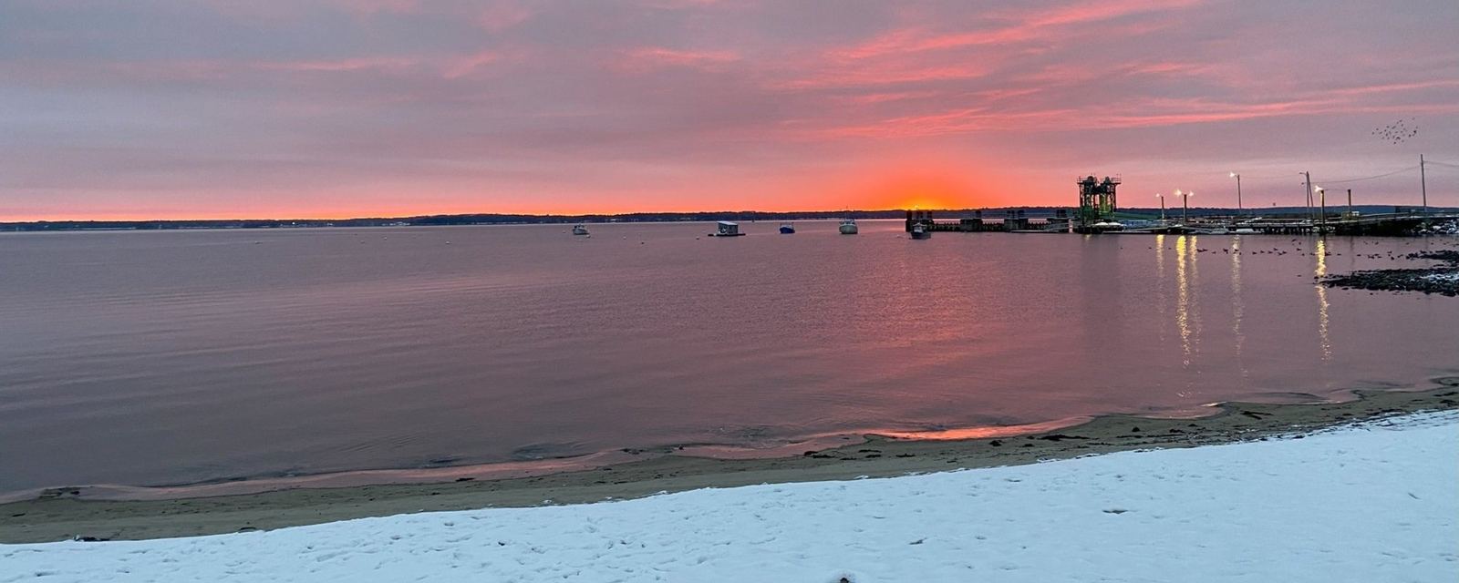Sunrise over a snowy Lincolnville Beach: pink sky, sand, boats and the ferry pier