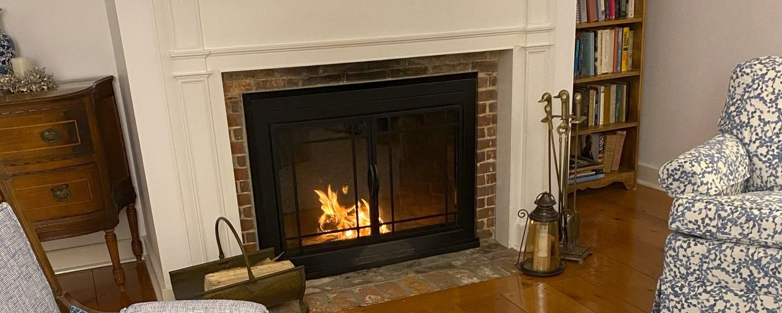 The commons room: a working fireplace with a brick hearth, iron doors, bookshelf and armchairs