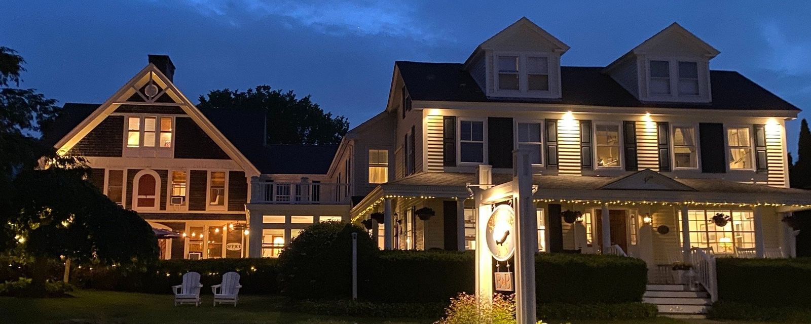 The inn lit up at night: glowing windows, the whale sign and Adirondack chairs