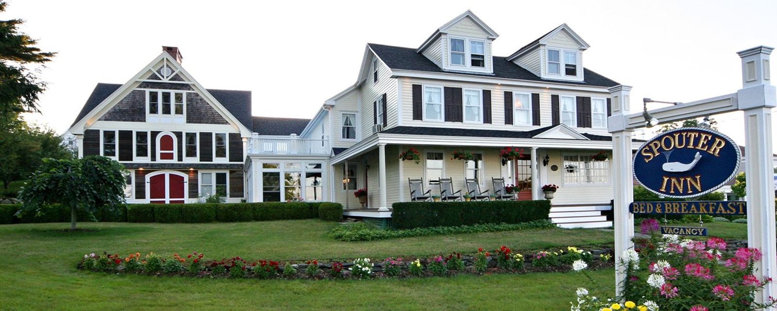 The Spouter Inn in daylight: SPOUTER INN sign, front-porch rocking chairs and tidy flower beds